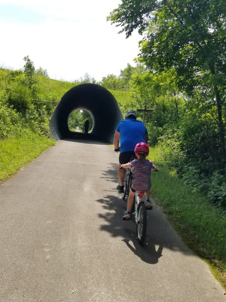 man and little girl riding bikes with a tunnel ahead of them