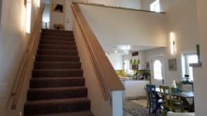 Stairway with wooden railings on both sides next to dining room & kitchen