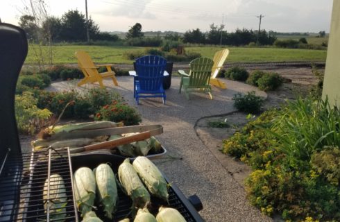 corn on a gas grill with patio beyond with colored patio chairs