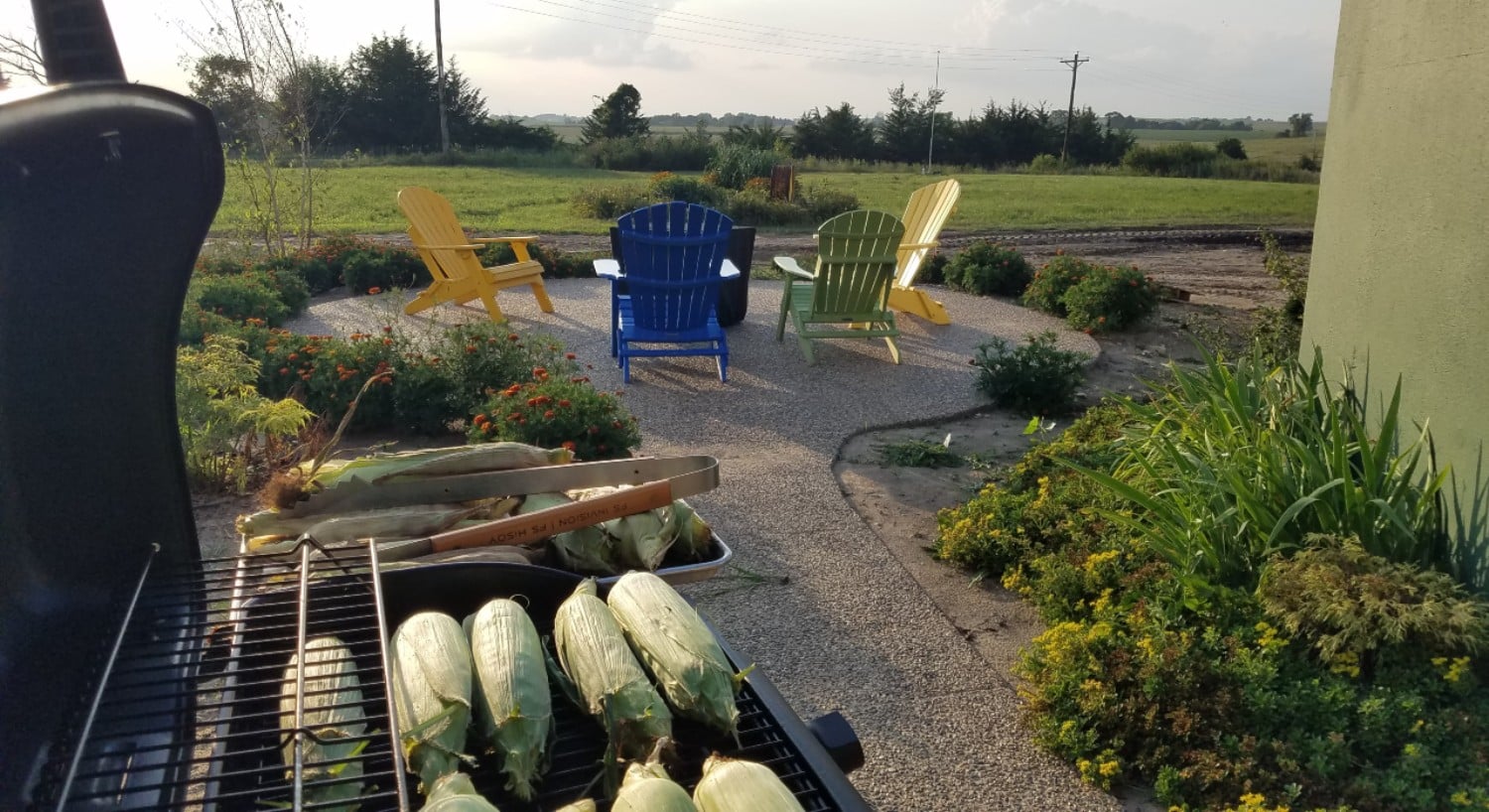 corn on a gas grill with patio beyond with colored patio chairs