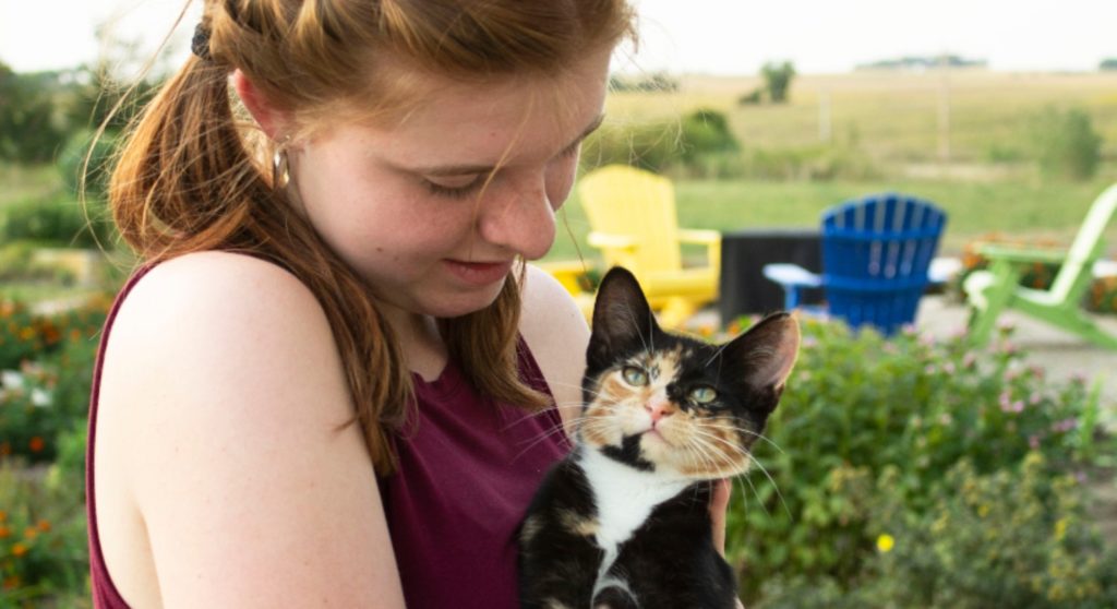 girl holding calico cat in garden