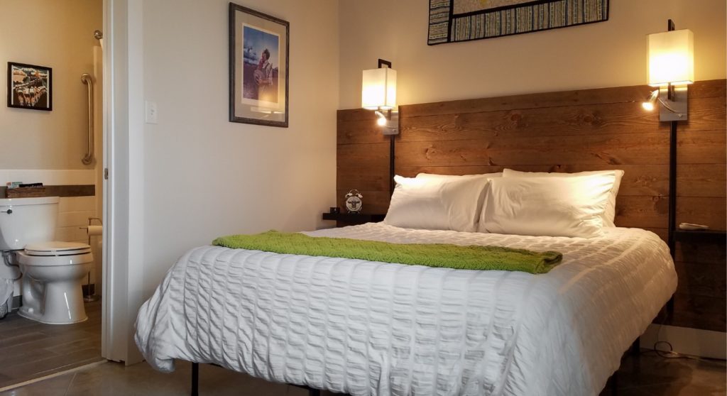 bed with white cover and lamps on wall beside it looking into bathroom with toilet