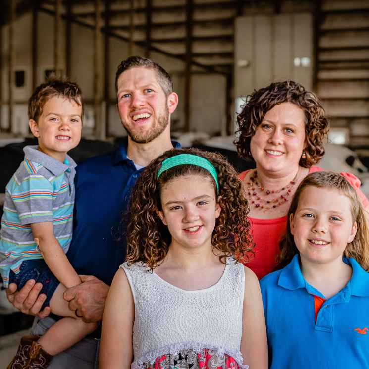 family with three children standing in a dairy barn
