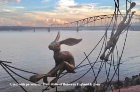 Metal sculpture of playful rabbits next to a body of water with a large bridge in the background