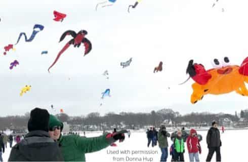 People with heavy coates flying multicolored kites in a field covered with snow