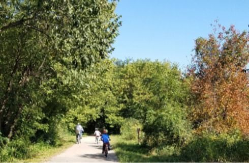 Bike path with surrounding trees with green and orange leaves with three people riding bikes