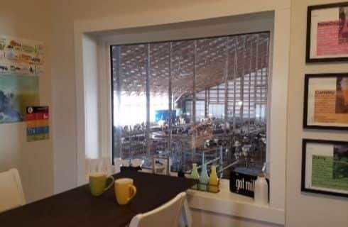 Room with a wooden table and chairs with a window overlooking dairy cow operations