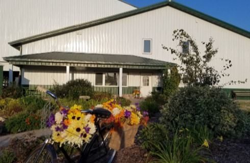 Outside view of the property painted white and green surrounded by lush green plants and bright flowers