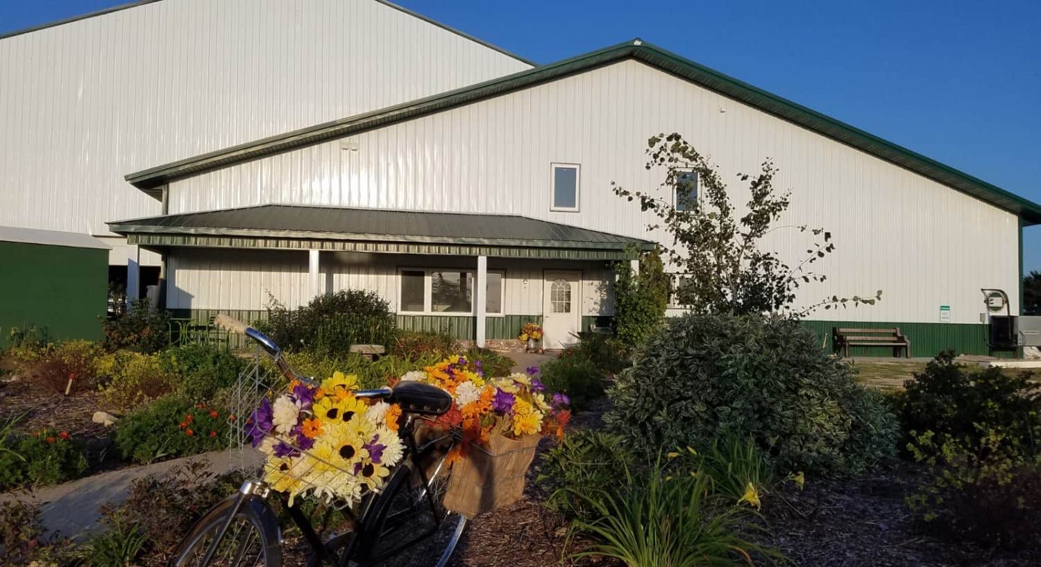 Outside view of the property painted white and green surrounded by lush green plants and bright flowers