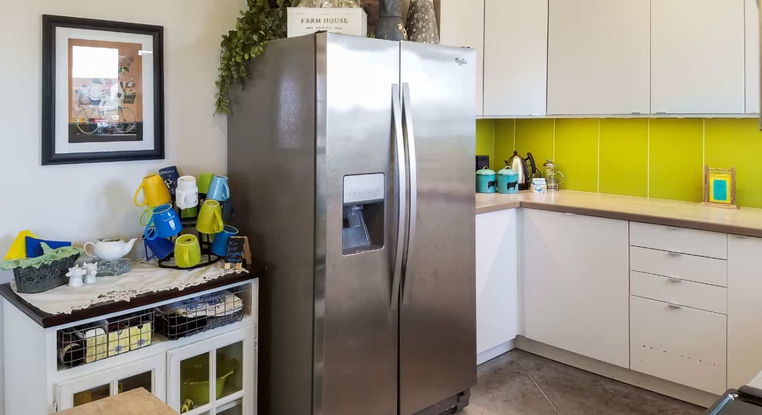 Kitchen with white walls, white cabinets, green backsplash, and stainless steel refridgerator