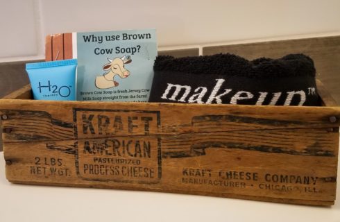 Close up view of old wooden crate filled with handmade soap, lotion, and black towel with the word makeup in white