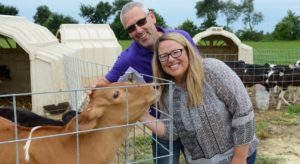 Man and woman smiling at the camera standing near a pen petting a brown cow