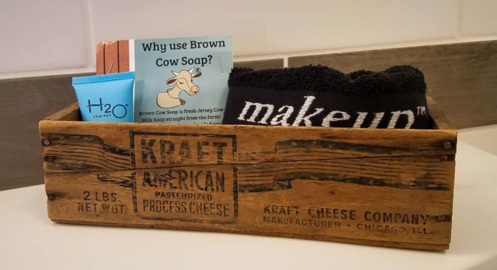 Close up view of old wooden crate filled with handmade soap, lotion, and black towel with the word makeup in white