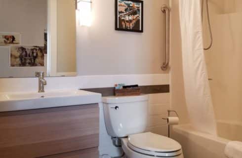 Bathroom with white walls and tile, white toilet, white sink, white shower and tub, white shower curtain, and large mirror