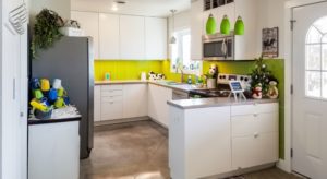 Large dining area and kitchen with wooden table and blue and yellow chairs, view to the outside, white cabinets, and light green backsplash