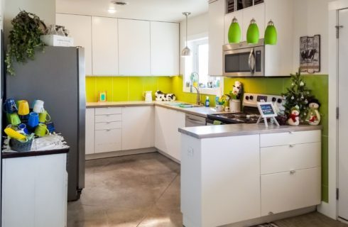 Large dining area and kitchen with wooden table and blue and yellow chairs, view to the outside, white cabinets, and light green backsplash