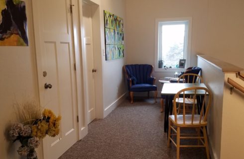 Loft area at the top of the stairs with white walls and trim, carpeting, small table with two chairs and small sitting area with a table and blue upholstered chairs