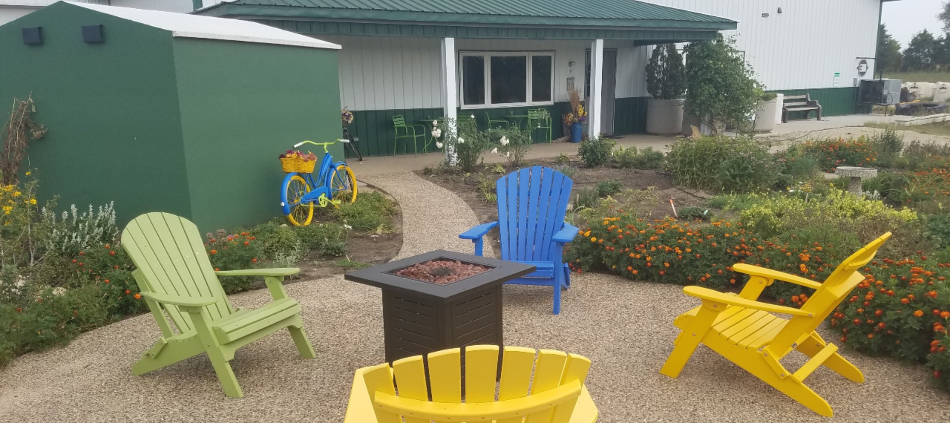 gas fire pit on concrete patio surrounded by 4 chairs beside a garden