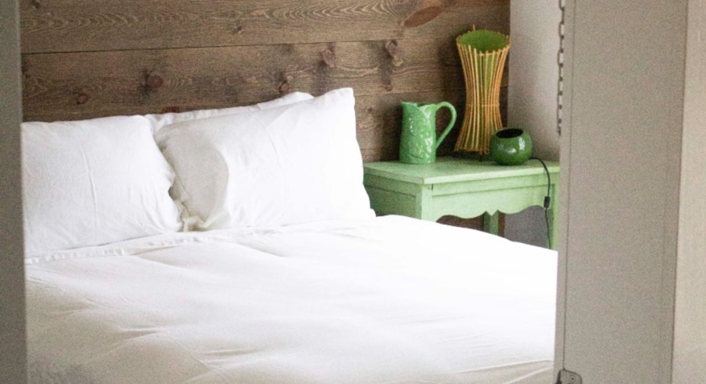 bed with white sheets with a green side table with green lamp