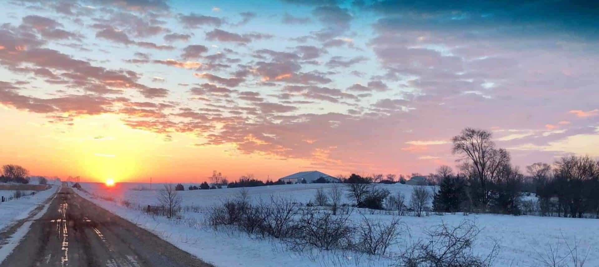 View of the farm with snow on the ground and the sun setting in the background