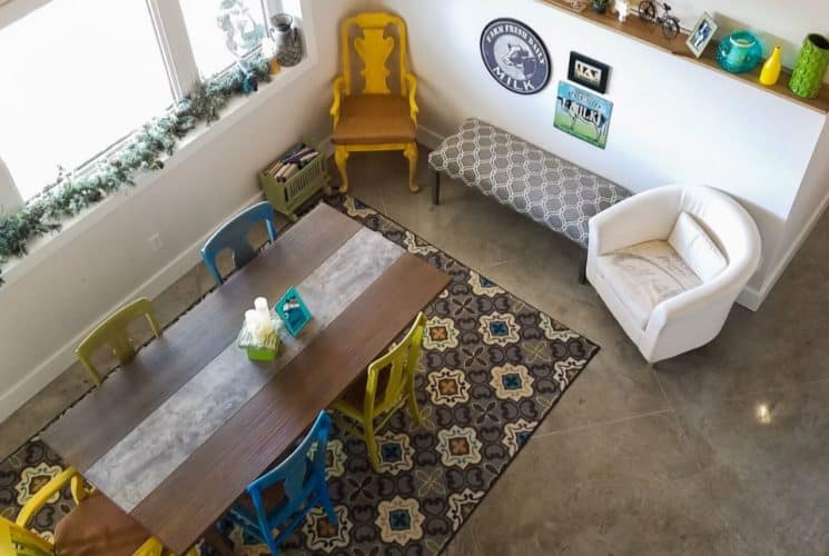 View of a dining area and sitting area from up high with large wooden table, blue and yellow chairs, large coordinating area rug, and upholstered bench and chair