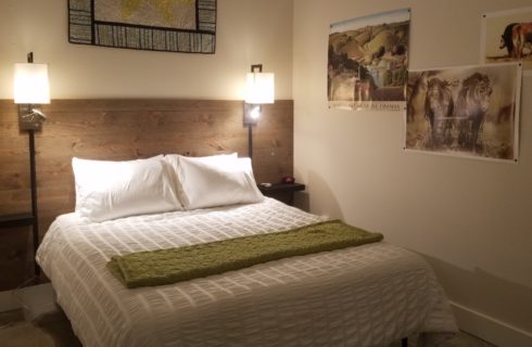 bed covered in white with lamps on wall beside, quilt above bed and posters on the wall of horses and countryside