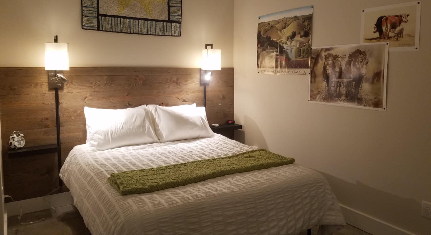 bed covered in white with lamps on wall beside, quilt above bed and posters on the wall of horses and countryside