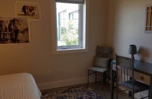 blue desk with lamp on top and 2 chairs with mirror above and window looking to outside with posters of horses on the wall