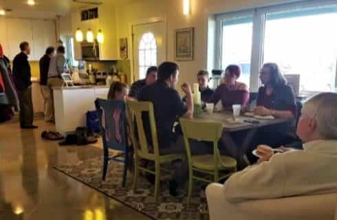 People gathered together in a dining and kitchen area eating and drinking