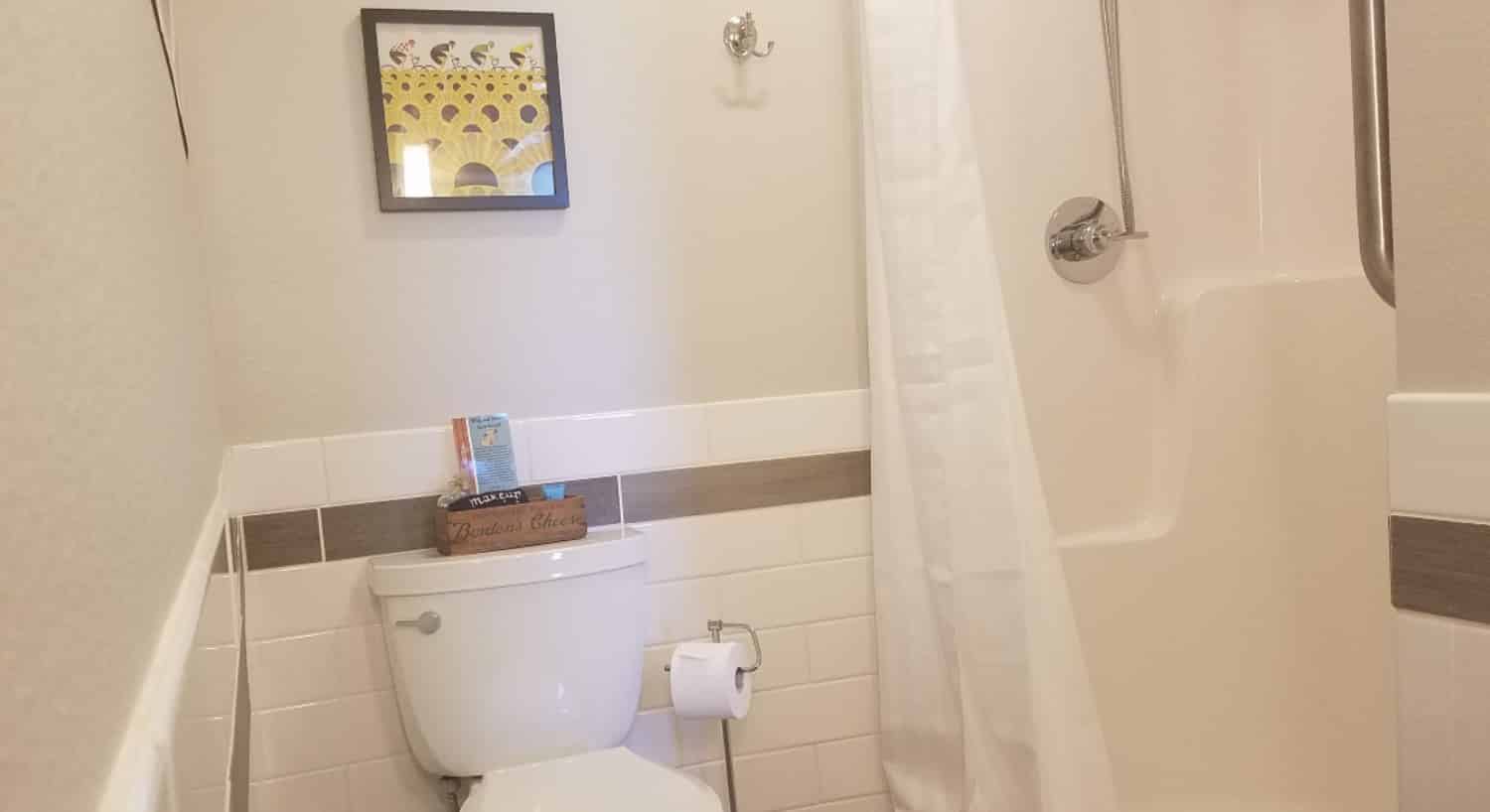 white toilet in modern bathroom with white tile half way up wall next to a walk-in shower with a white shower curtain