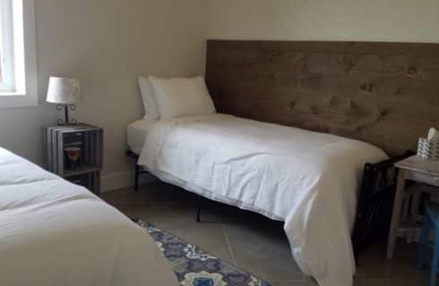 2 twin beds covered in white sheets with crates as and end table and a white desk with a blue chair