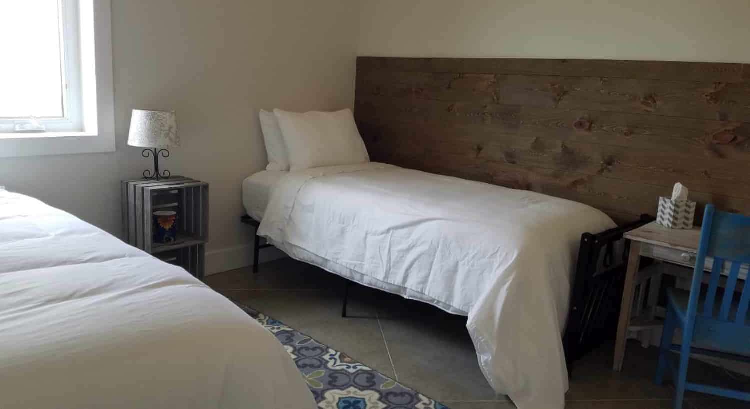 2 twin beds covered in white sheets with crates as and end table and a white desk with a blue chair